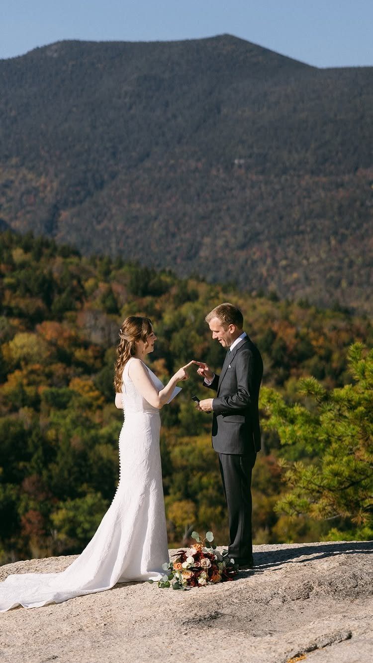Bride and groom standing on a rocky cliff overlooking autumn mountains during wedding.