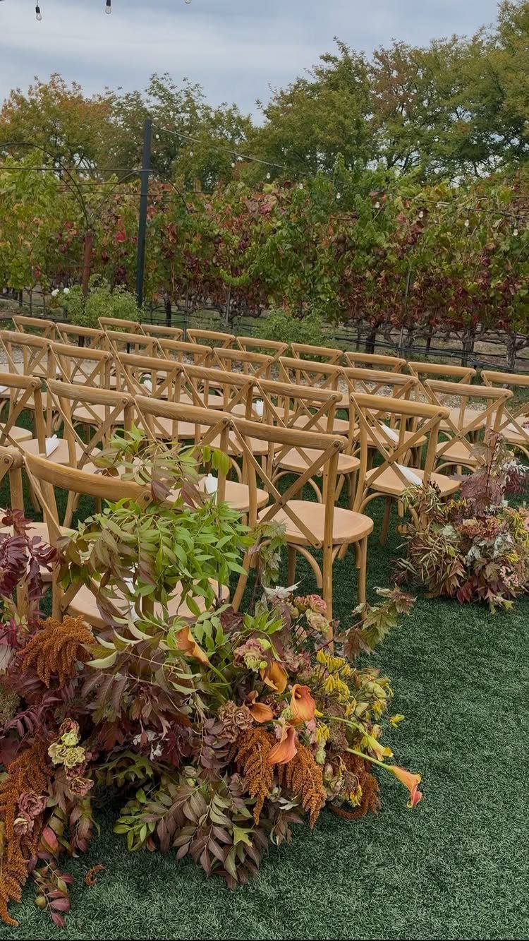 Wooden ceremony chairs on a green lawn with autumn flowers and vineyards.