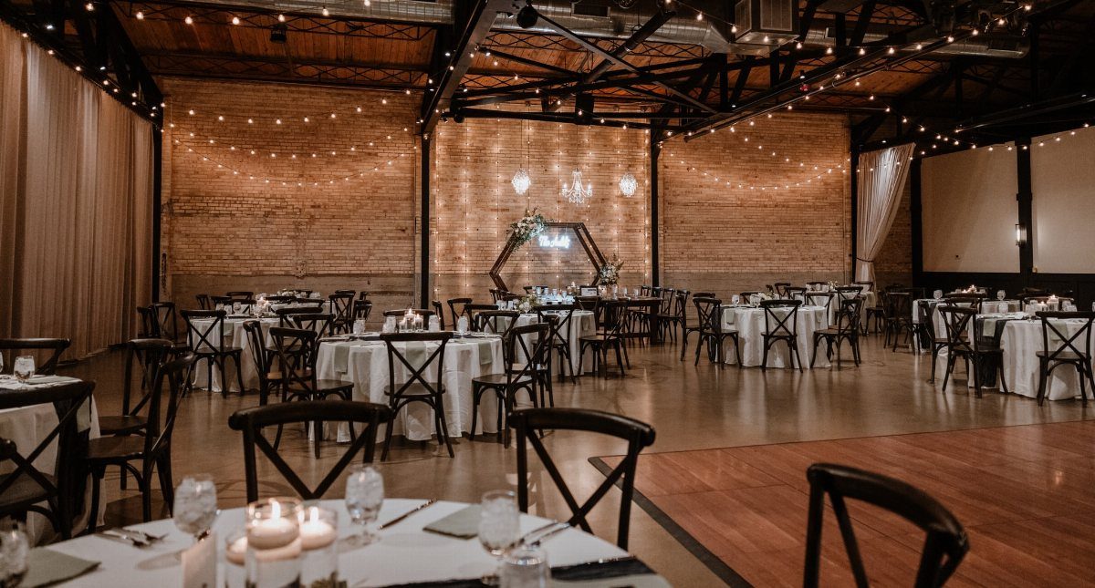 Dream Wedding Venue Ideas: 11 Places to Say I Do 9 Rustic event venue with white clothed tables, black chairs, and warm string lighting.
