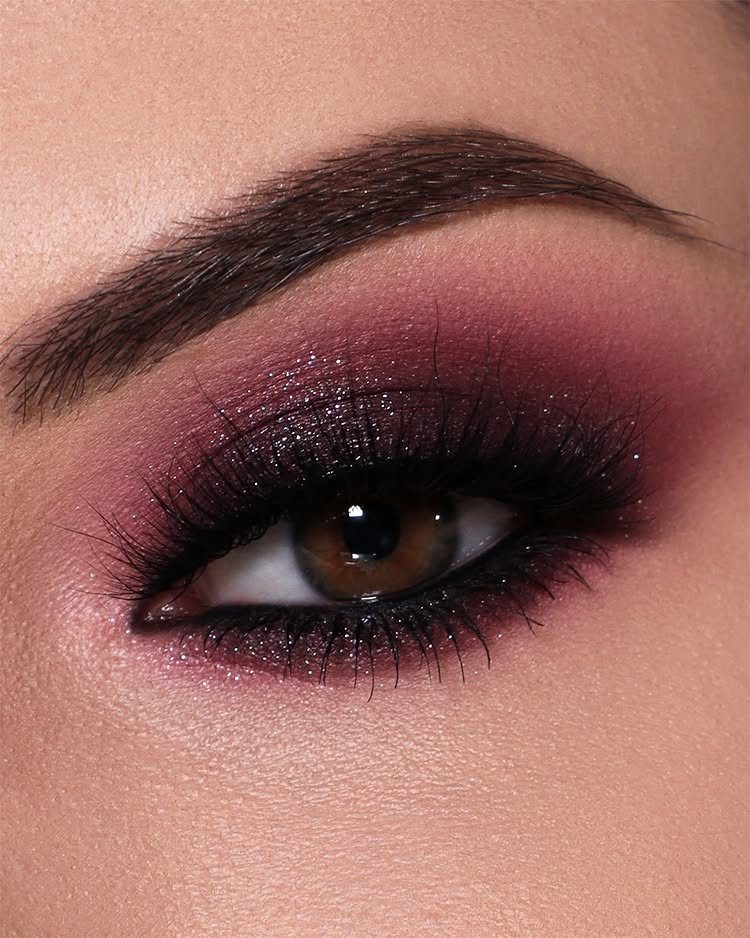 Eye with deep burgundy glitter eyeshadow and long dark lashes.