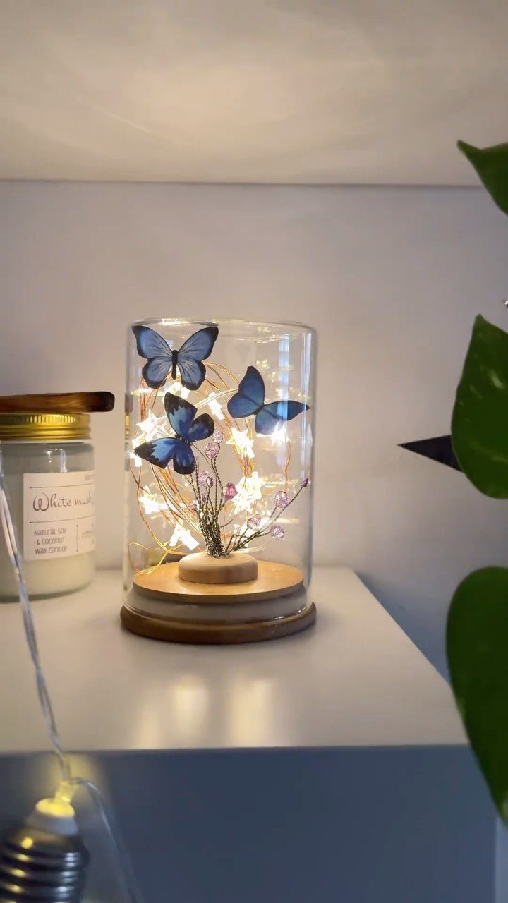 Glass cloche with blue butterflies and glowing fairy lights on a wooden base.