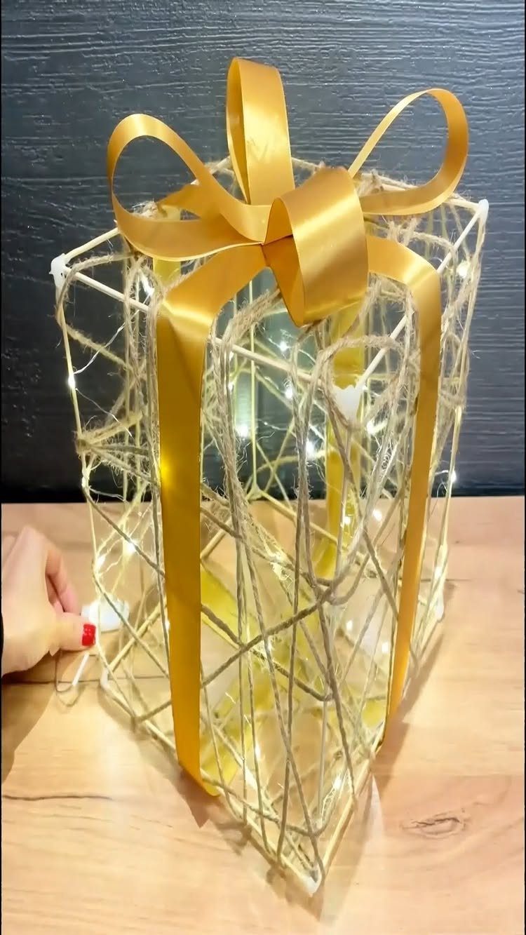 Gold metal gift-shaped lantern with fairy lights and a large gold ribbon bow.