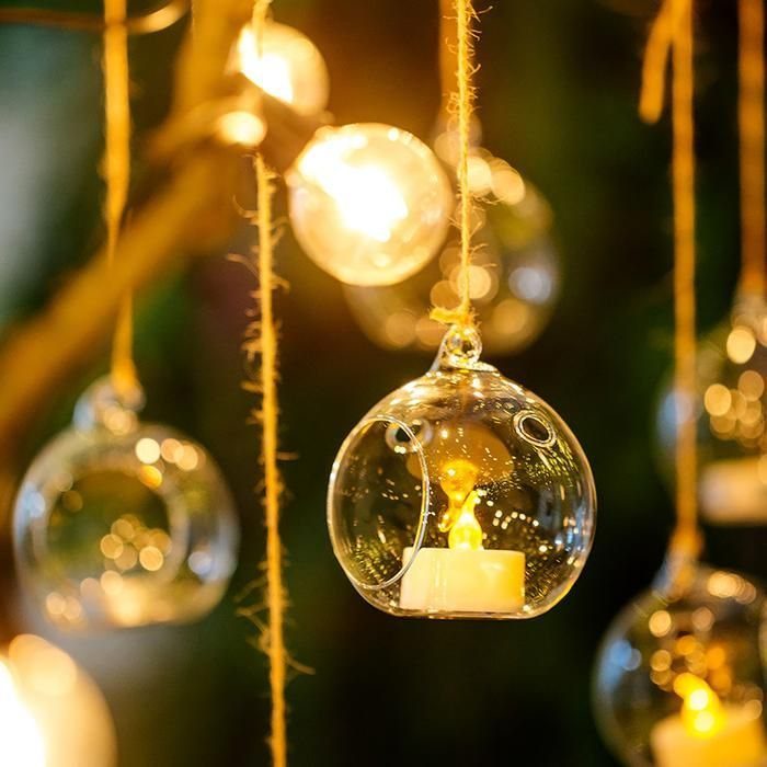Spherical glass tea light holders hanging from tree branches with glowing white candles.