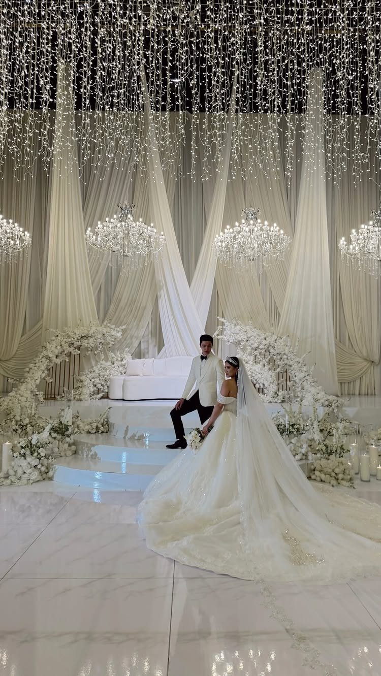 Bride and groom posing under a ceiling of shimmering white fairy lights and chandeliers