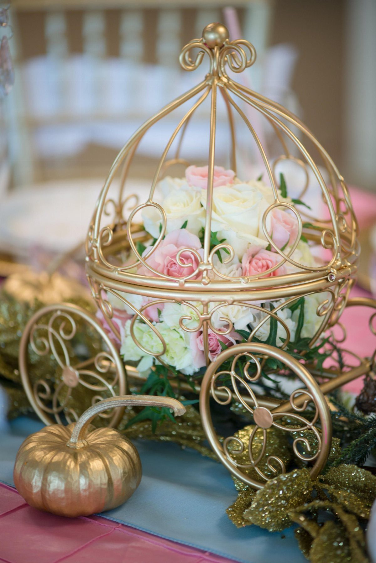Gold pumpkin carriage filled with pink and white roses and a small gold pumpkin.