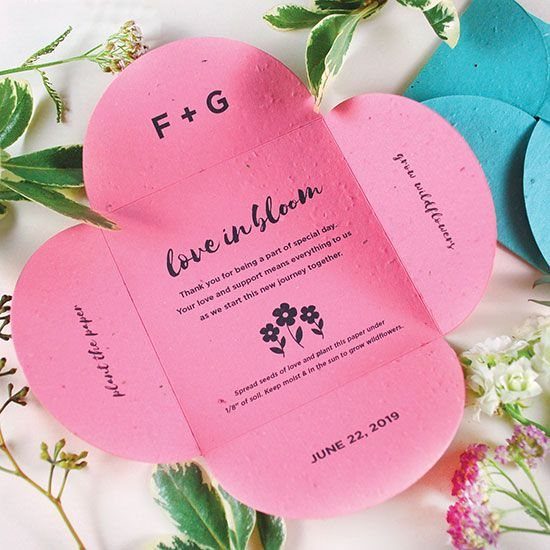 Pink flower-shaped seed paper wedding favor with text and surrounding fresh flowers.