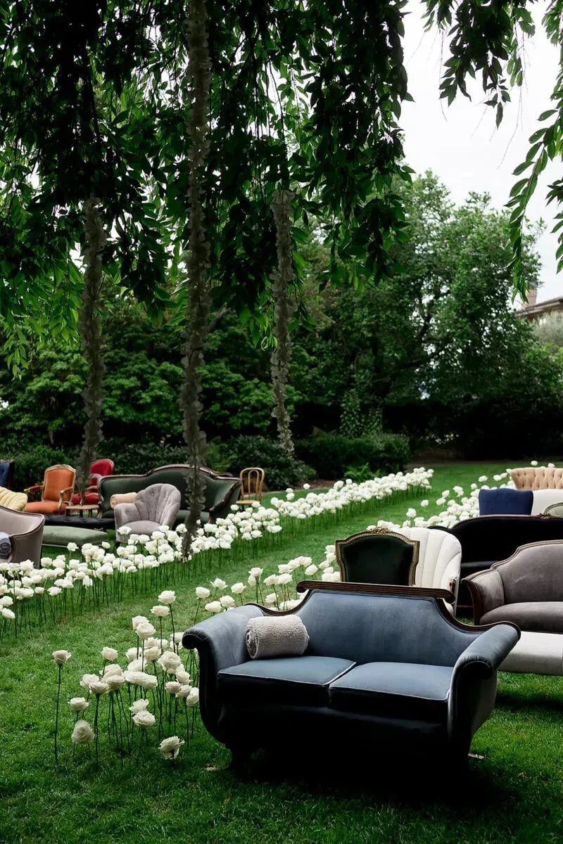 Vintage sofas and armchairs arranged on a green lawn with white flowers.