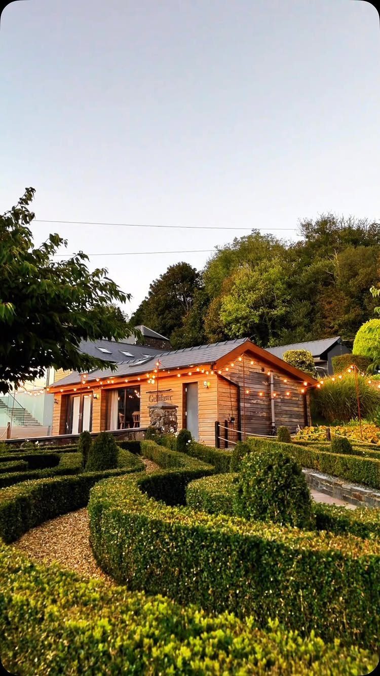 Fantasy Wedding Venue Ideas: 11 Storybook Settings 8 Wooden building with string lights behind a green boxwood hedge maze and trees.