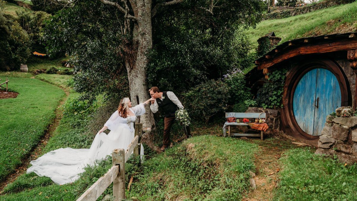 Fantasy Wedding Venue Ideas: 11 Storybook Settings 7 Bride and groom kissing in front of a round blue door in a grassy hill.
