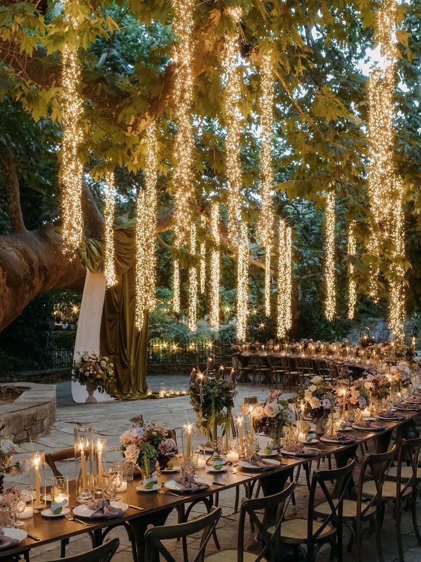Fantasy Wedding Venue Ideas: 11 Storybook Settings 5 Outdoor wedding reception table under a tree with cascading fairy lights and floral centerpieces.