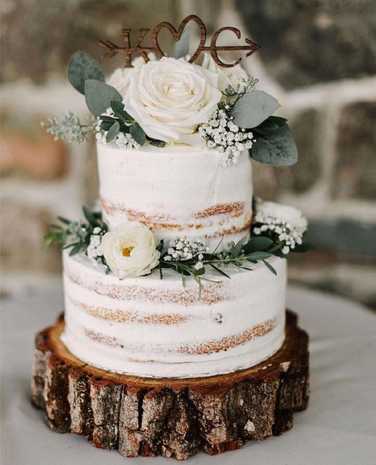 Flat Wedding Cakes: 6 Ideas for Simple, Low Tiers 3 Two-tier naked wedding cake with white flowers on a rustic wooden log slice.
