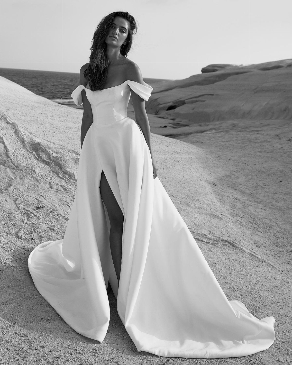 Woman in an off-the-shoulder satin wedding gown with a high slit in a desert.