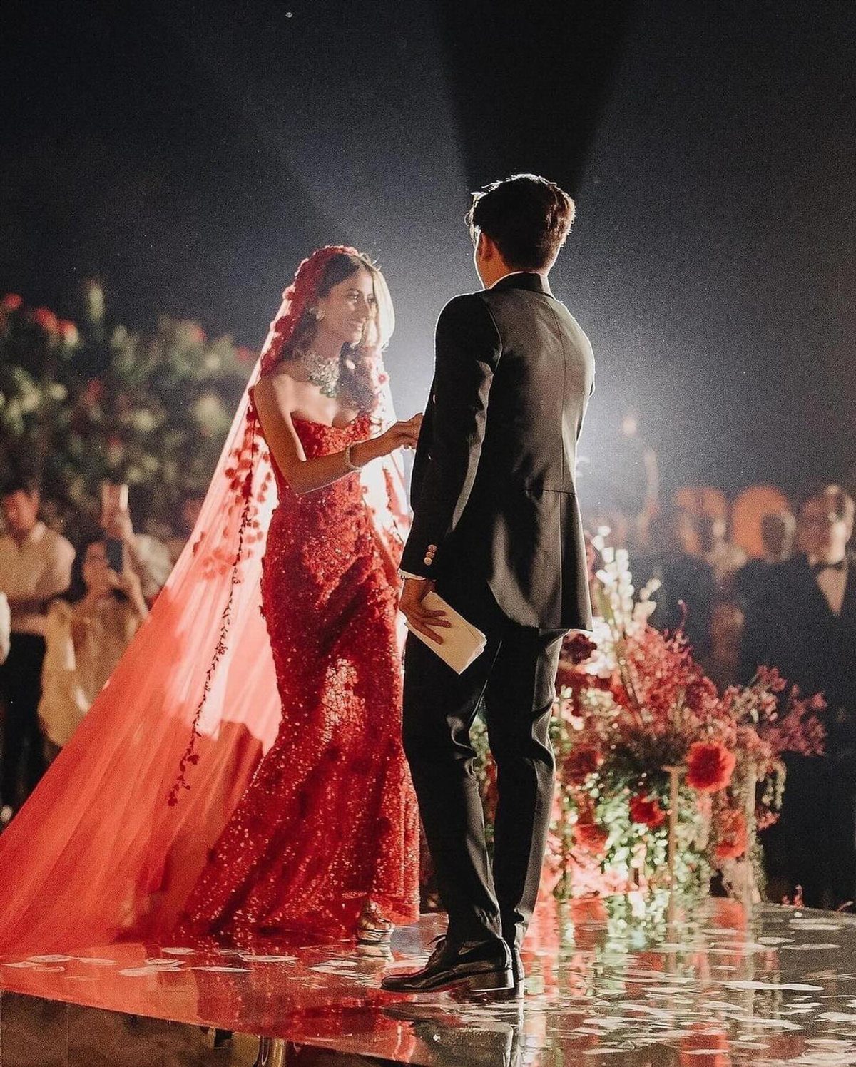 Woman in red sequined gown and veil facing man in black suit.