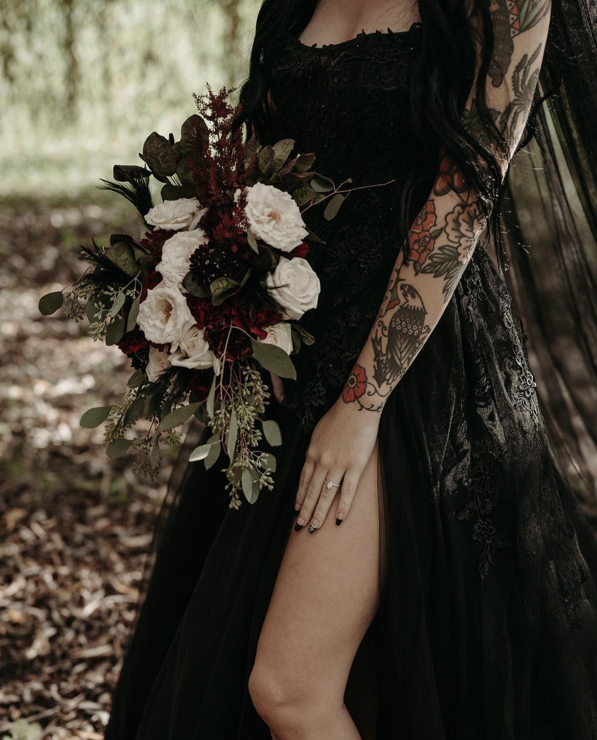 8 Gothic Romance Wedding Ideas for a Dark, Moody Day 4 Person in a black lace wedding dress holding a red and white rose bouquet.