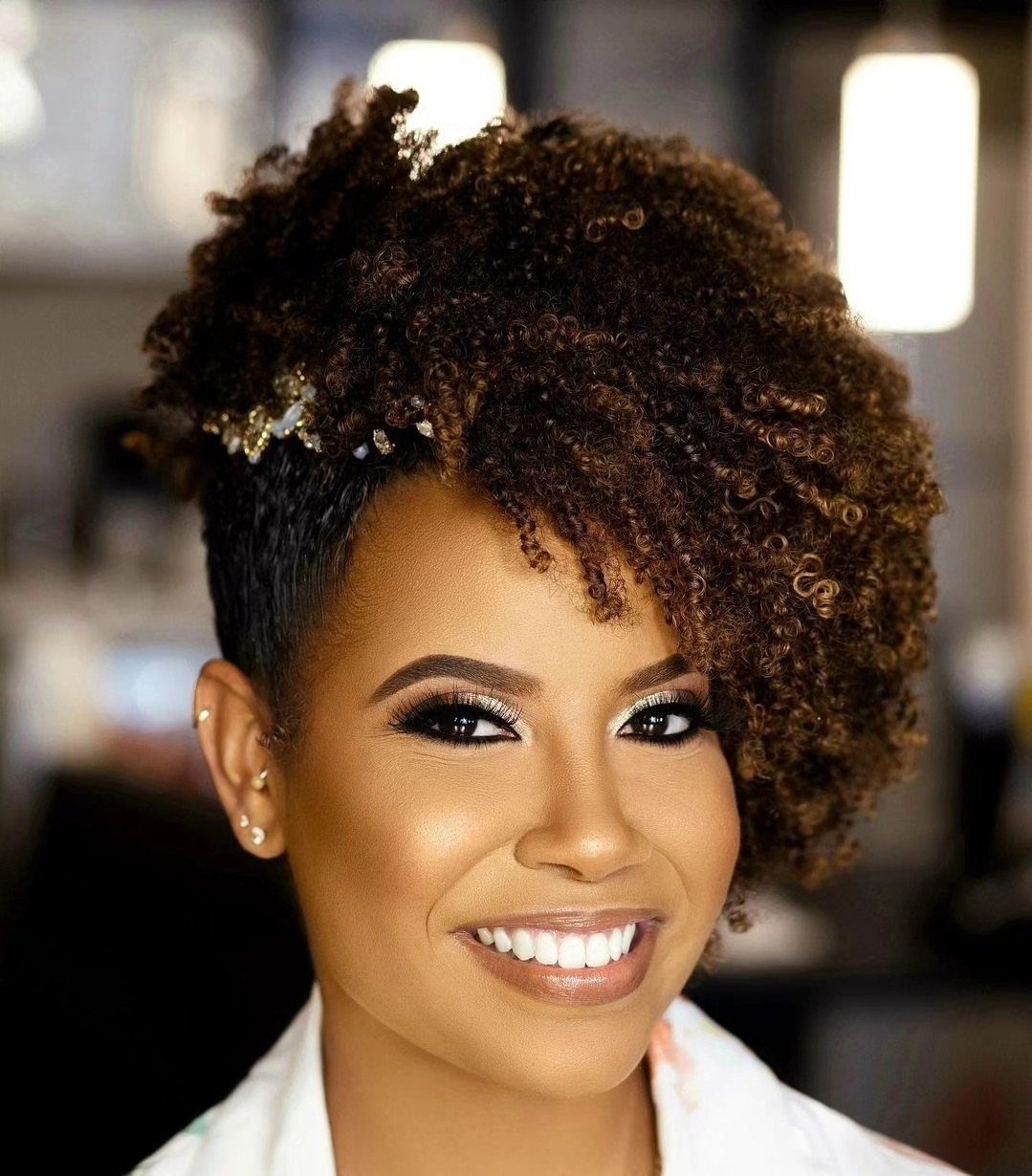 14 Ideas for Hair for a Wedding Guest, From Buns to Waves 9 Woman with a voluminous curly brown afro featuring small gold hair accessories.