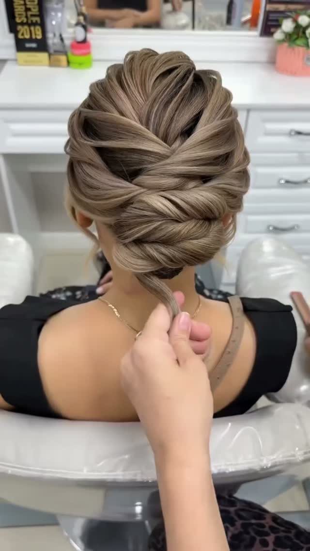 14 Ideas for Hair for a Wedding Guest, From Buns to Waves 1 Intricate low chignon updo on a woman with light brown hair in a salon.