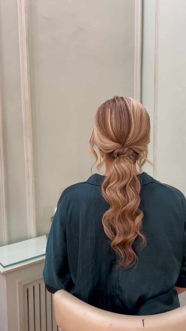14 Ideas for Hair for a Wedding Guest, From Buns to Waves 7 Woman with long wavy blonde hair styled in a loose low ponytail.