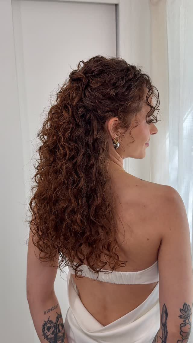 11 Half Up and Down Wedding Hair Ideas for Brides 3 Woman with curly reddish-brown hair in a half-up style wearing a white dress.