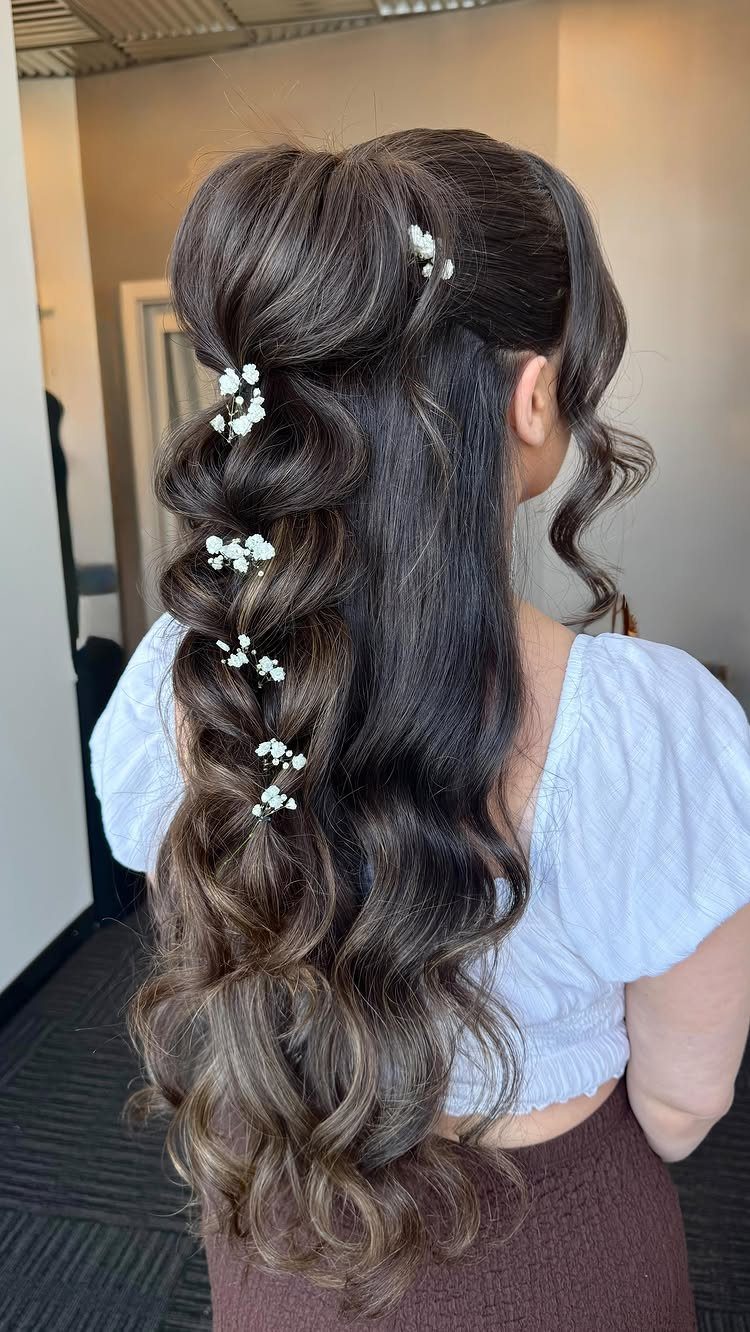 Long wavy brown hair in a half-updo decorated with small white flowers.