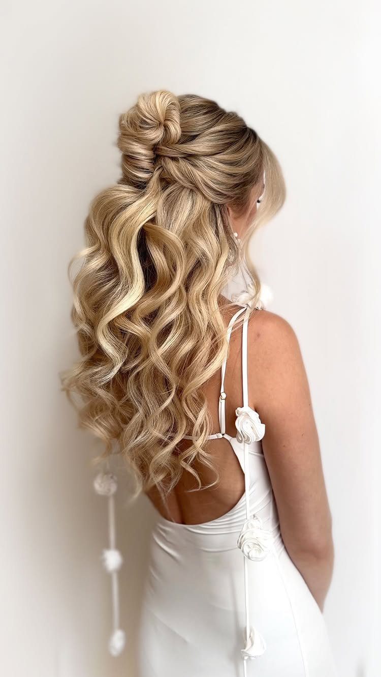 Blonde woman with a half-up bun and long voluminous curls wearing a white dress.