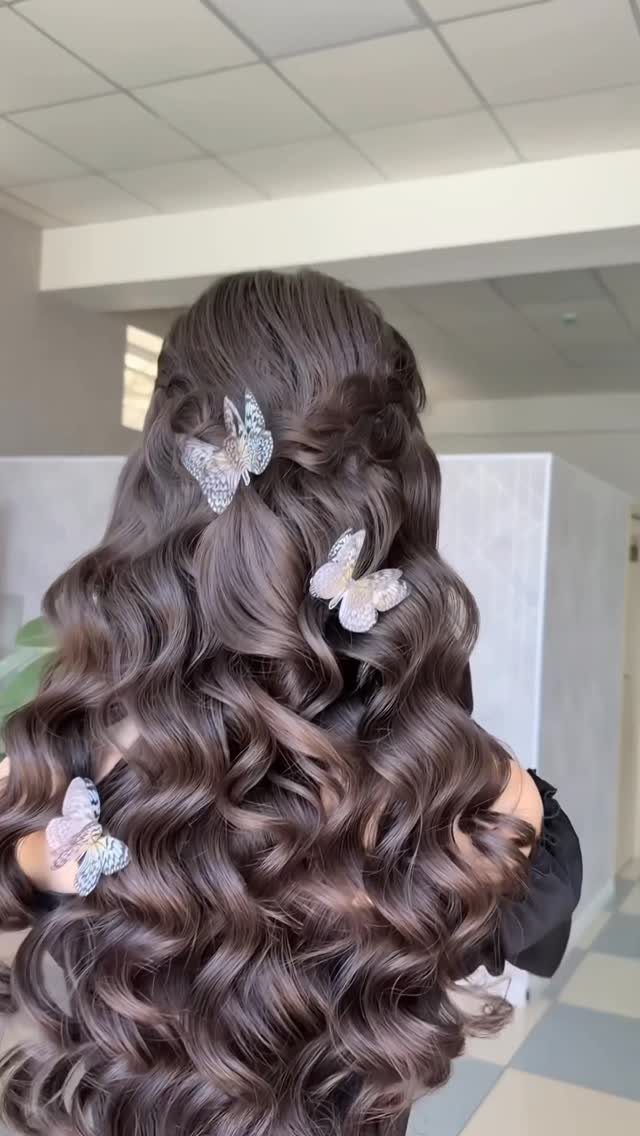 Long brown voluminous curls in a half-updo with decorative butterfly hair clips