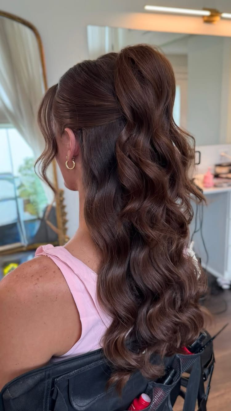 Woman with long brown hair in a high half-up ponytail with voluminous curls.