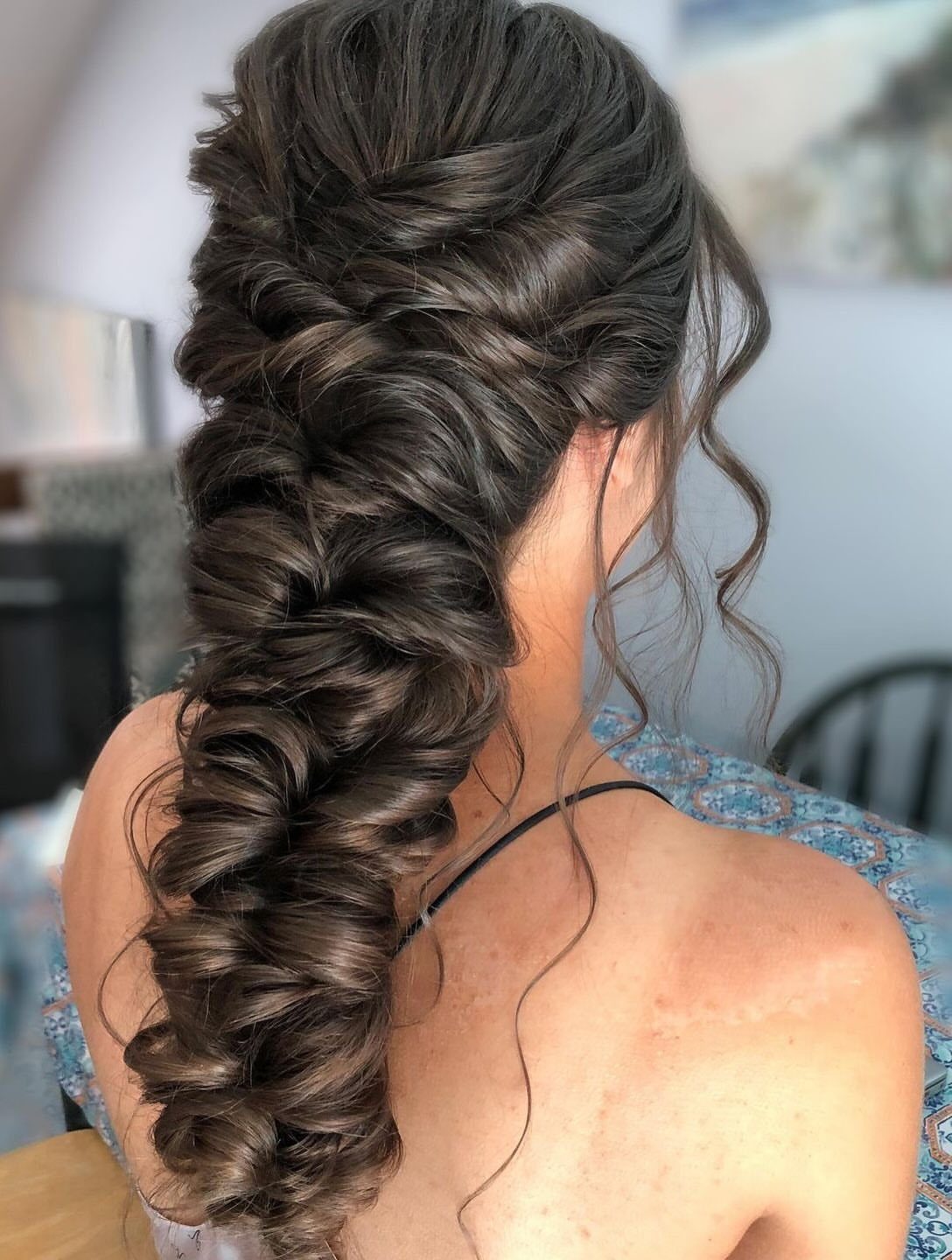 Long dark brown hair styled in a thick, loose, textured braid cascading down the back.