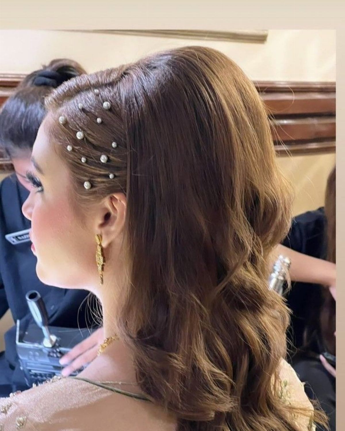 Woman with long wavy brown hair in a half-updo with pearl hair pins.