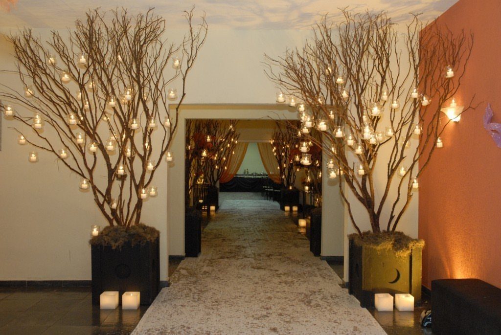 Leafless brown branches in planters decorated with small hanging glass candles in a hallway