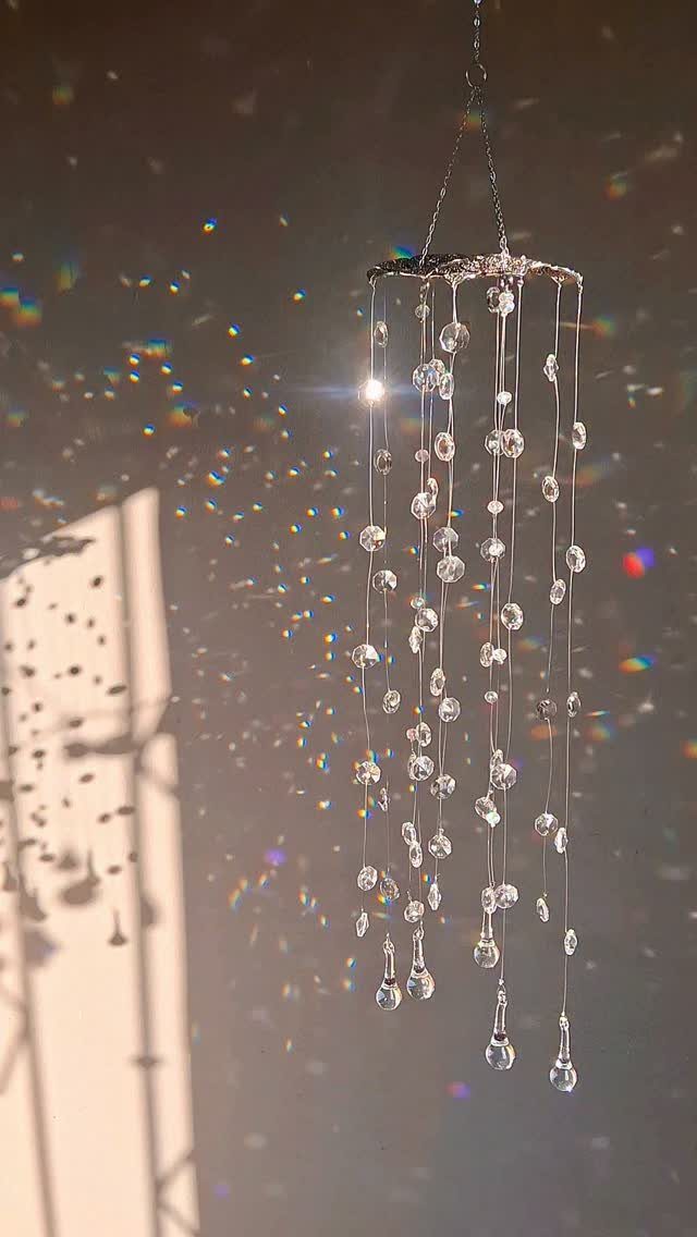 Hanging crystal suncatcher with faceted glass beads reflecting light against a dark wall.