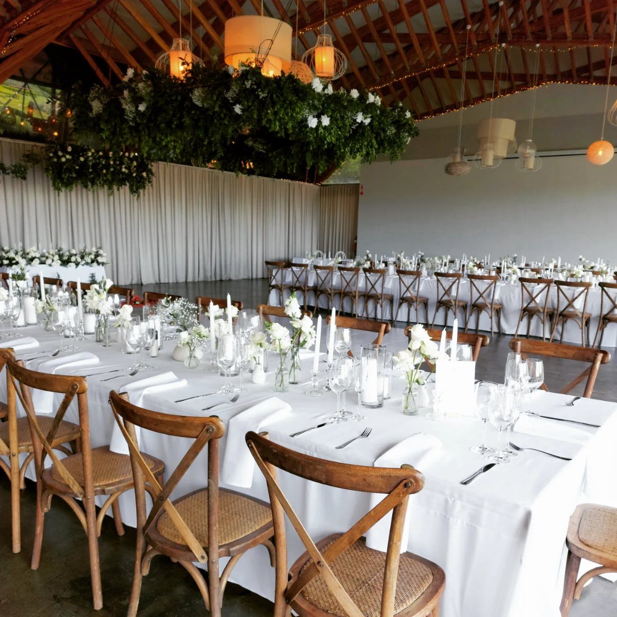 Wedding reception table setting with a large hanging floral chandelier and orange lanterns.