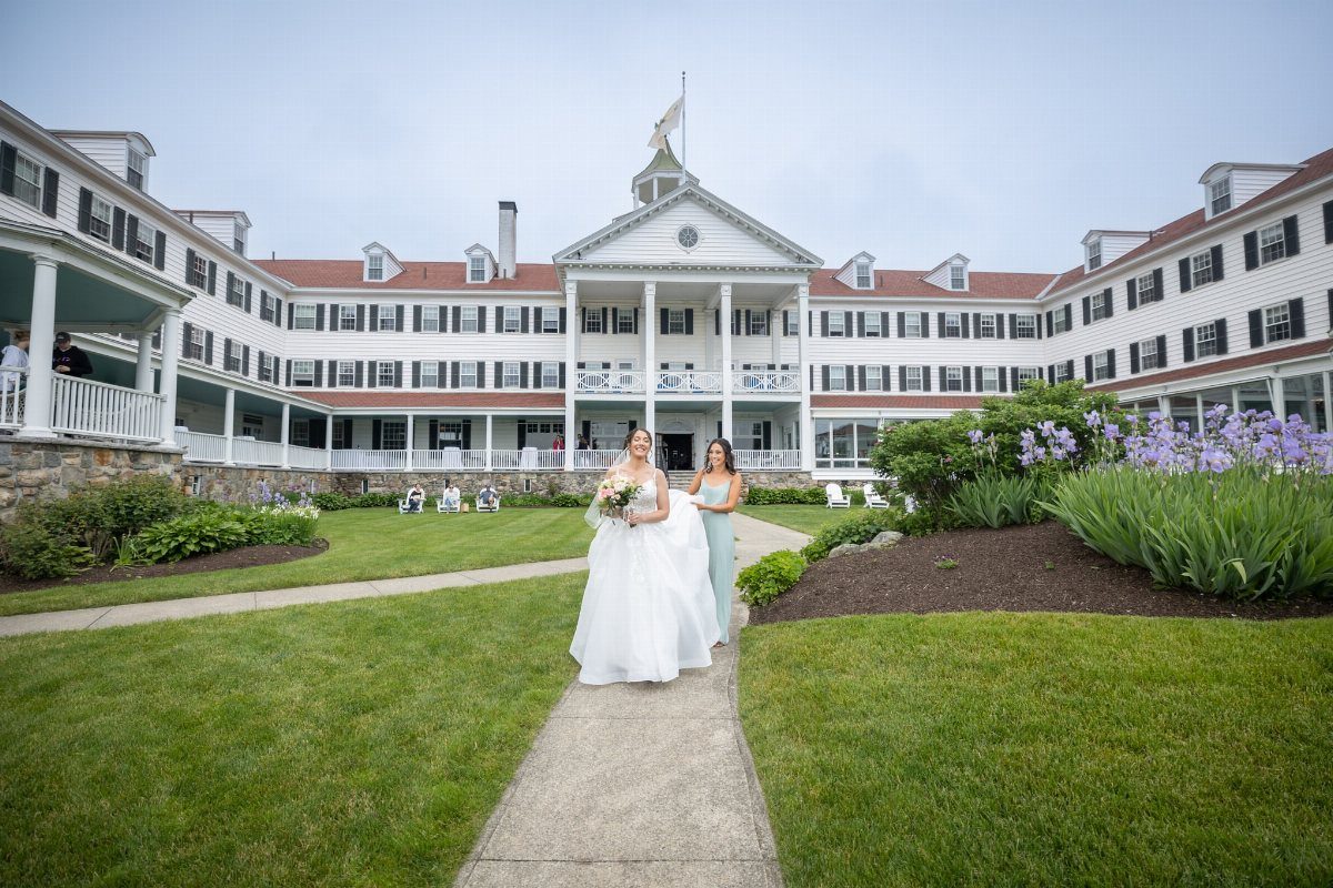 Bride and bridesmaid walking on a path in front of a large white hotel.