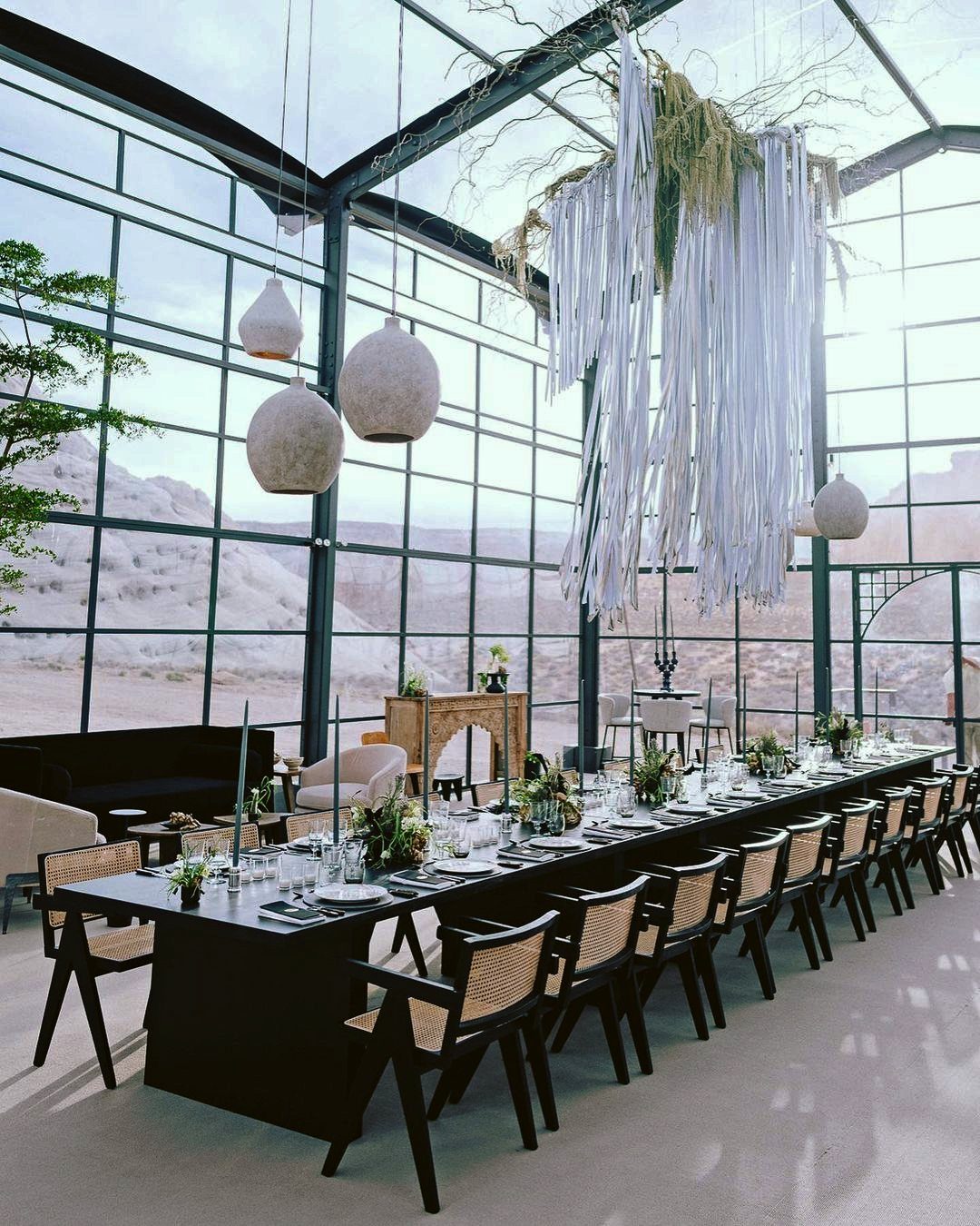Long black dining table in a glass pavilion overlooking a rocky desert landscape.