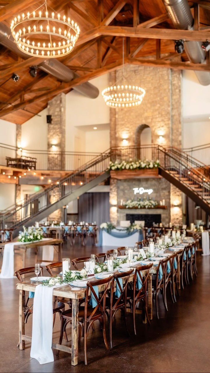 Grand event hall with wooden beams, stone walls, and long decorated banquet tables.