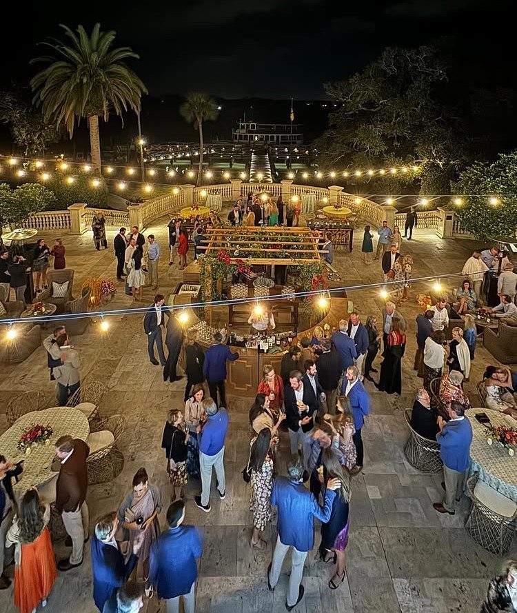 Outdoor evening wedding reception on a stone terrace with guests and string lights.