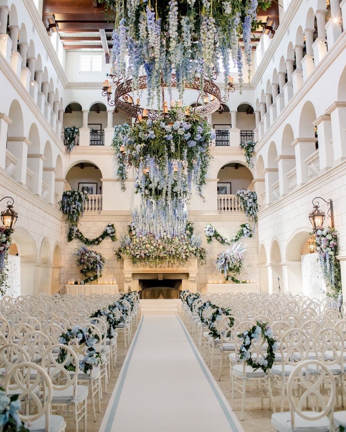 Grand indoor wedding ceremony space with white chairs and cascading blue floral arrangements.
