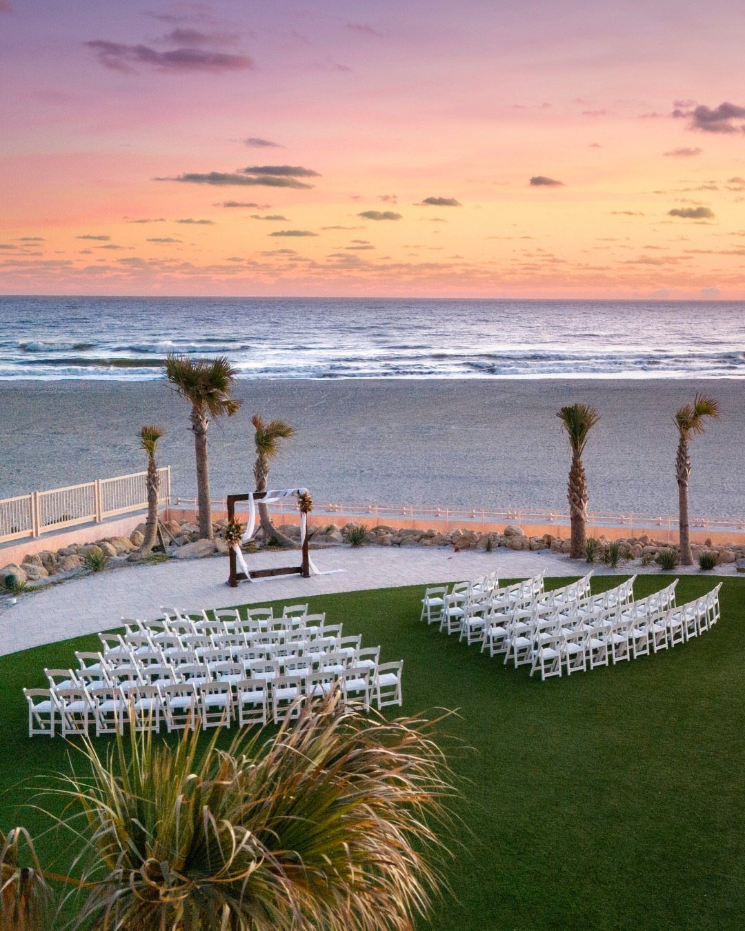 Wedding ceremony setup with white chairs and arch on a lawn by the ocean.