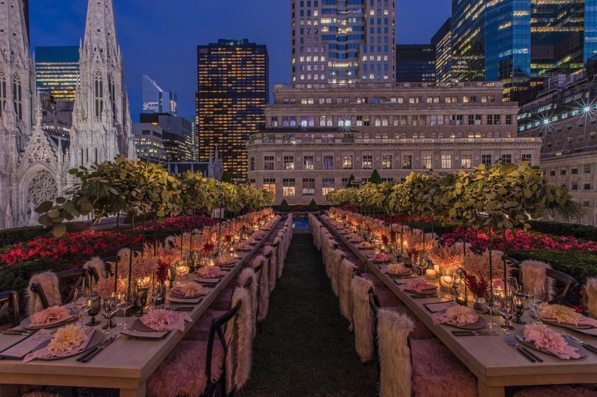 Rooftop garden dining setup with long tables and city skyscrapers in the background.
