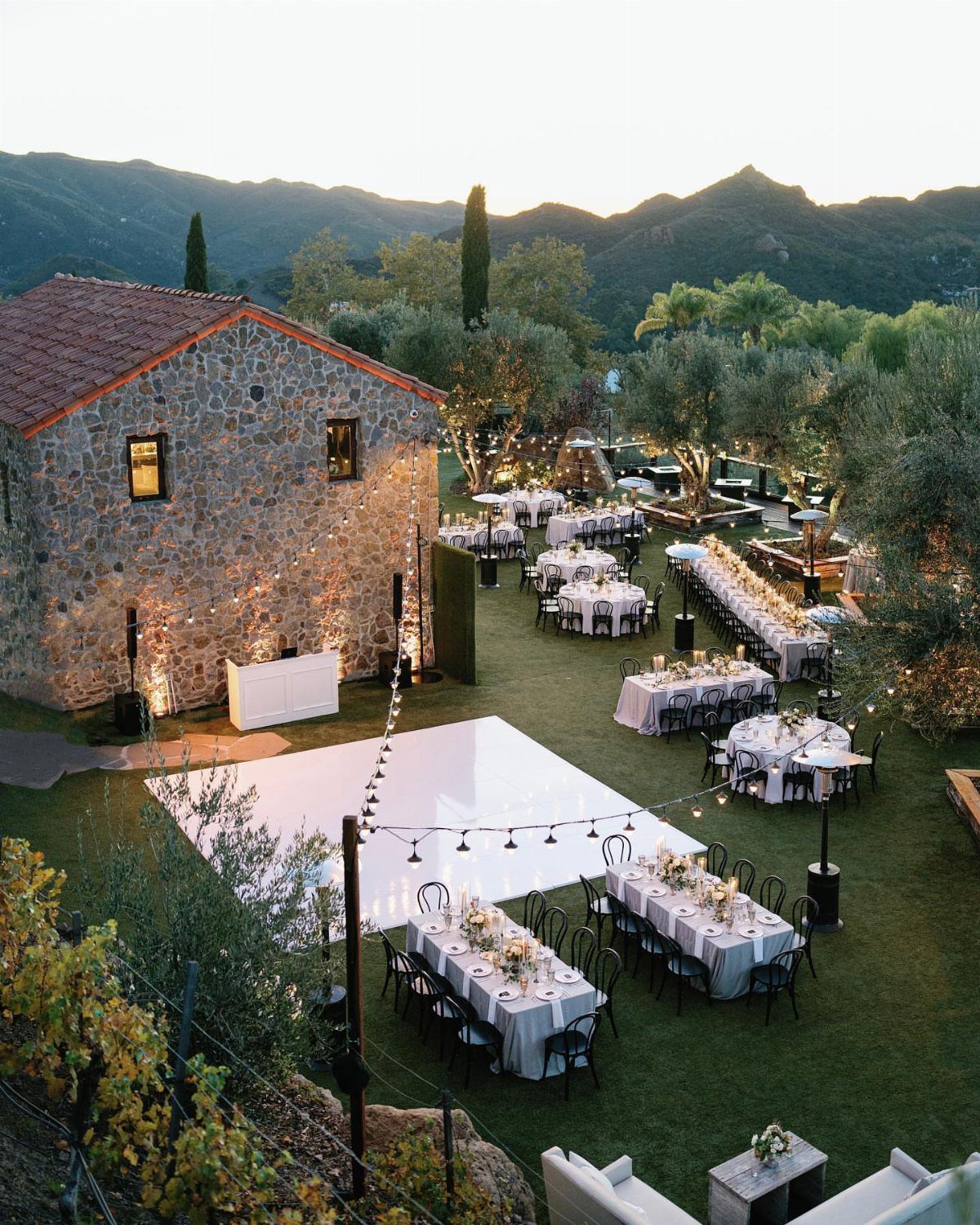 Stone estate wedding venue with white tables and dance floor against mountain backdrop