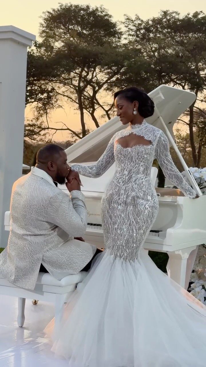 Woman in a sparkling ivory mermaid wedding dress posing with a man by a piano.
