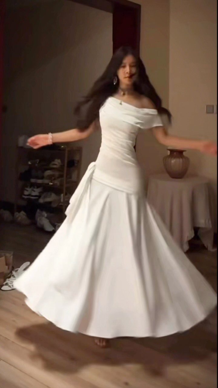Woman in a white off-the-shoulder mermaid wedding dress posing in a room.