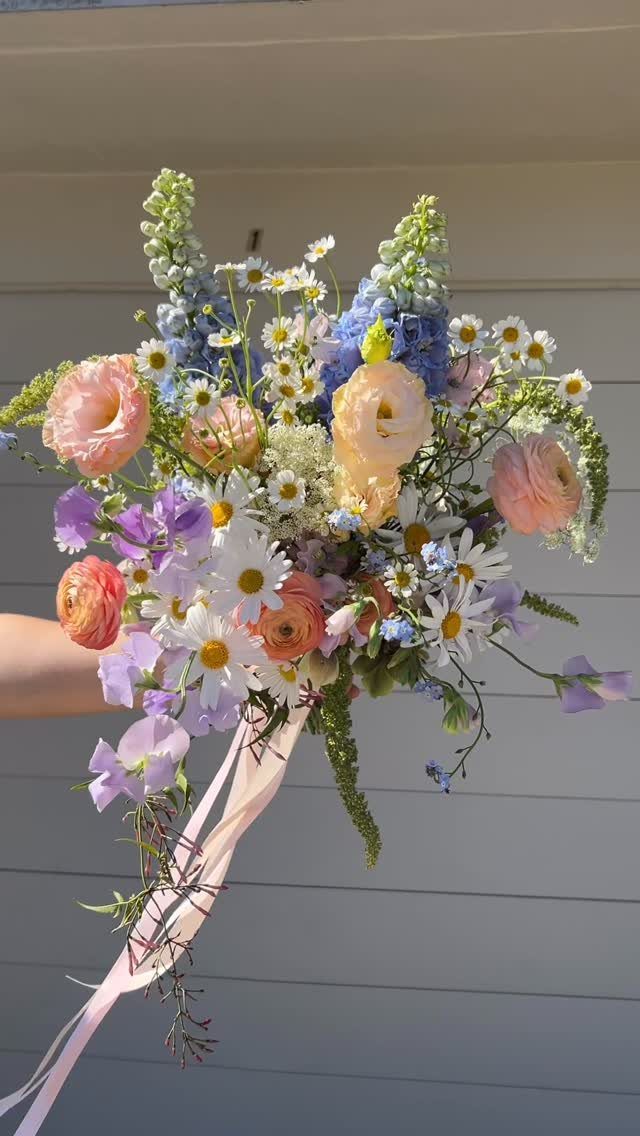 Floral wedding bouquet with light pink ranunculus, white daisies, and blue delphiniums.