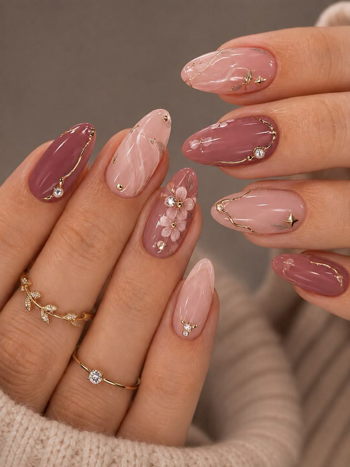 Light pink and mauve almond nails with gold accents and small 3D flowers.