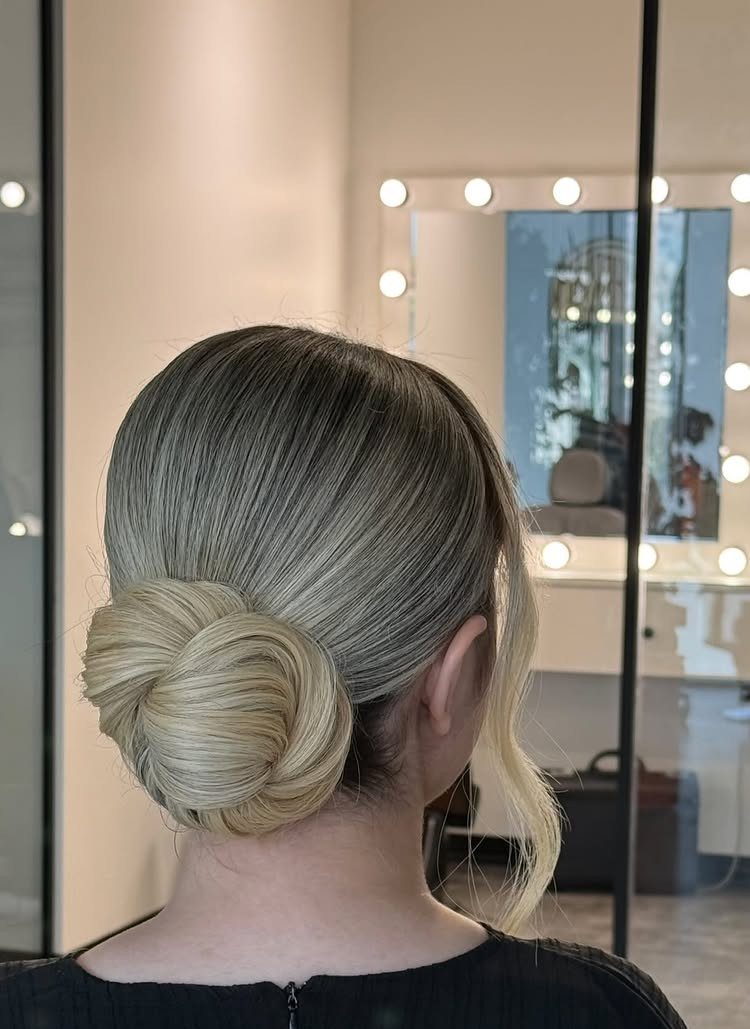 15 Long Hair Wedding Styles for Braids, Buns and Waves 2 Blonde hair styled in a sleek low bun in a bright salon setting.