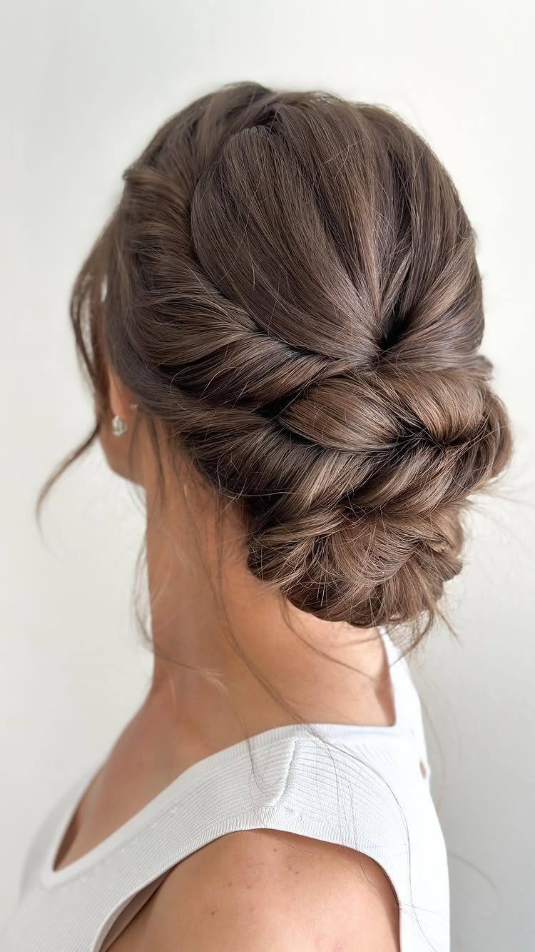 15 Long Hair Wedding Styles for Braids, Buns and Waves 3 Brown hair styled in a low twisted bun with intricate braided details.