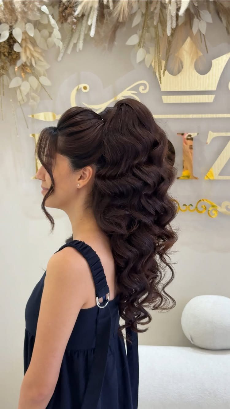 15 Long Hair Wedding Styles for Braids, Buns and Waves 10 Woman with a high volume-packed ponytail featuring large cascading curls in dark brown hair.