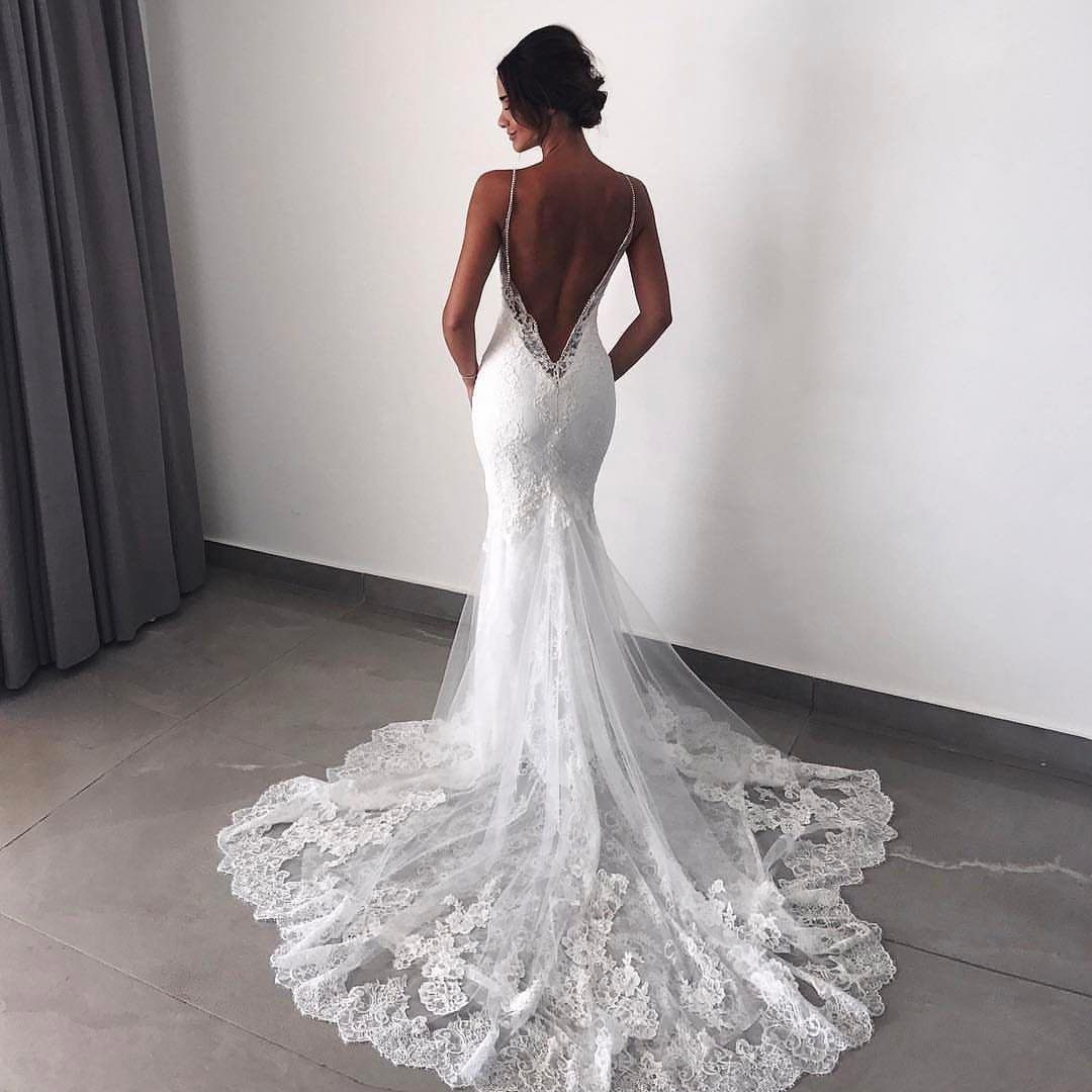 Woman wearing a white lace wedding dress with a deep open back and train.