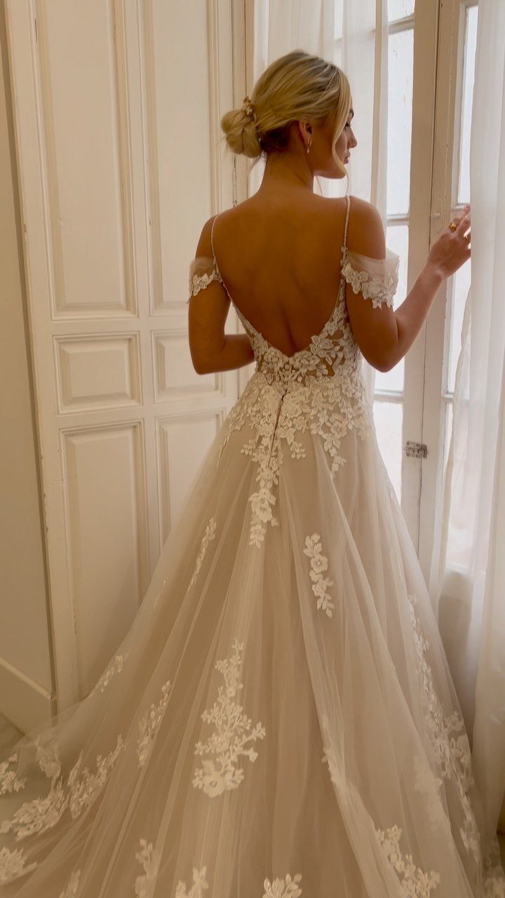 Woman from behind in a white off-the-shoulder lace wedding dress by a window