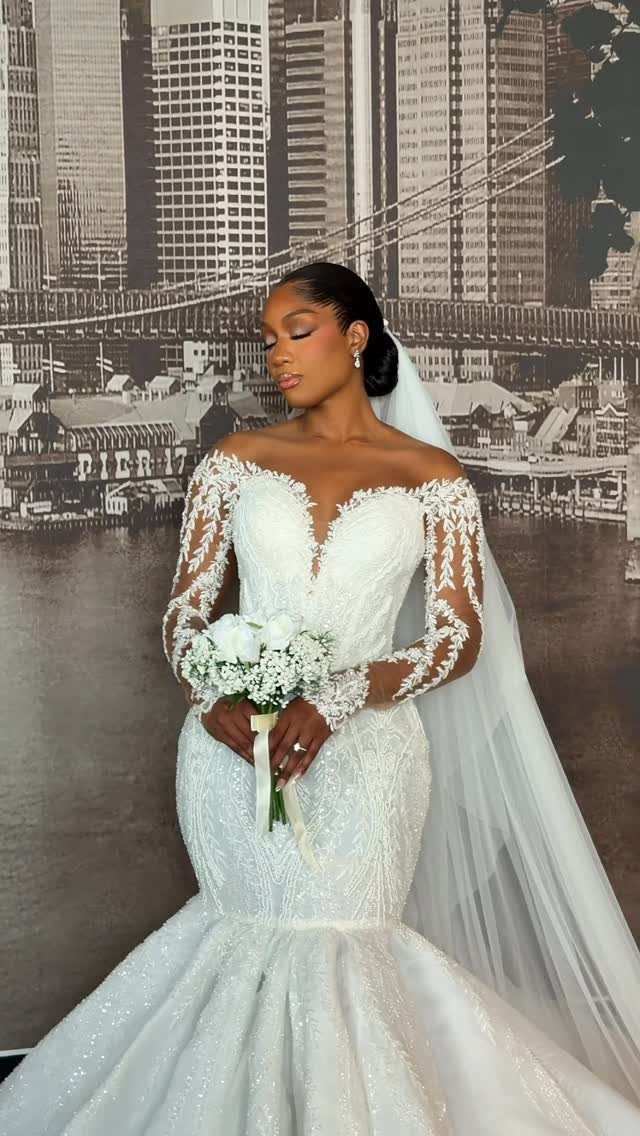Woman in a lace wedding dress wearing pearl earrings and holding a white bouquet.