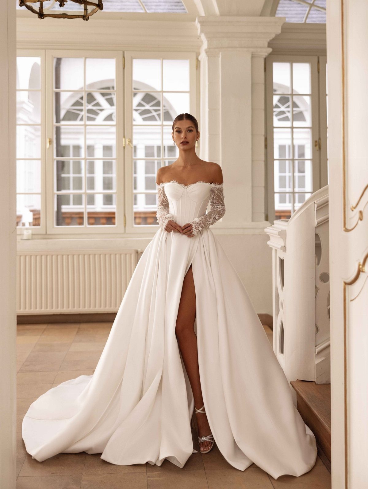 Woman in off-the-shoulder white wedding dress with lace sleeves and high leg slit.